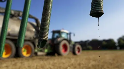 Traktor syns i bakgrunden i solljus. I förgrunden syns slangar.